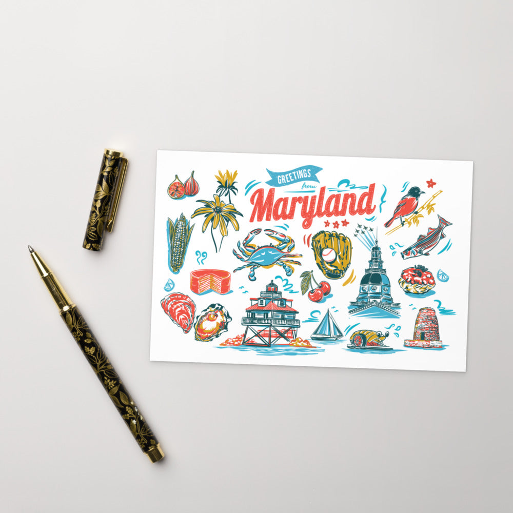 A flat-lay photograph of a 'Greetings, Maryland' art print card, styled with a gold and black patterned pen on a light gray background.