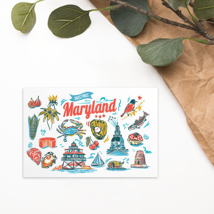 A white greeting card featuring a colorful hand-drawn illustration of Maryland landmarks, food, and nature, styled on a white surface with brown paper and green leaves.