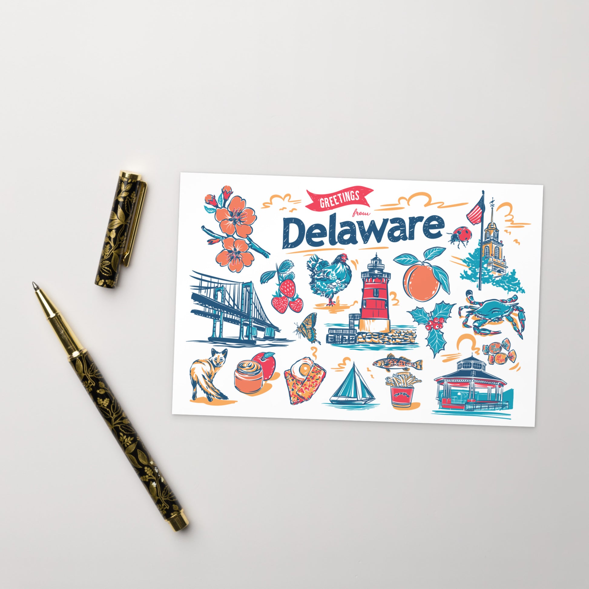 A flat-lay photograph of a 'Greetings from Delaware' art print card, styled with a gold-patterned pen and pen cap on a light gray background.
