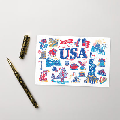 A white rectangular art print featuring colorful USA-themed illustrations and the word 'USA' in large blue letters, styled on a light gray surface with a gold-and-black pen and its cap beside it.